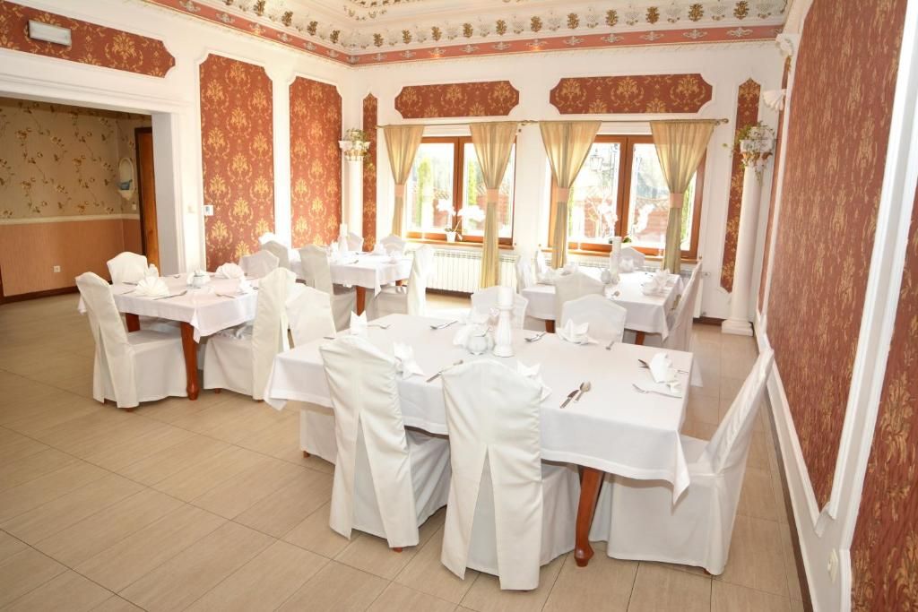 Une salle de banquet dotée de nombreuses tables rondes, chacune recouverte d’une nappe blanche et entourée de chaises, et ornée d’un plafond décoratif aux motifs floraux.