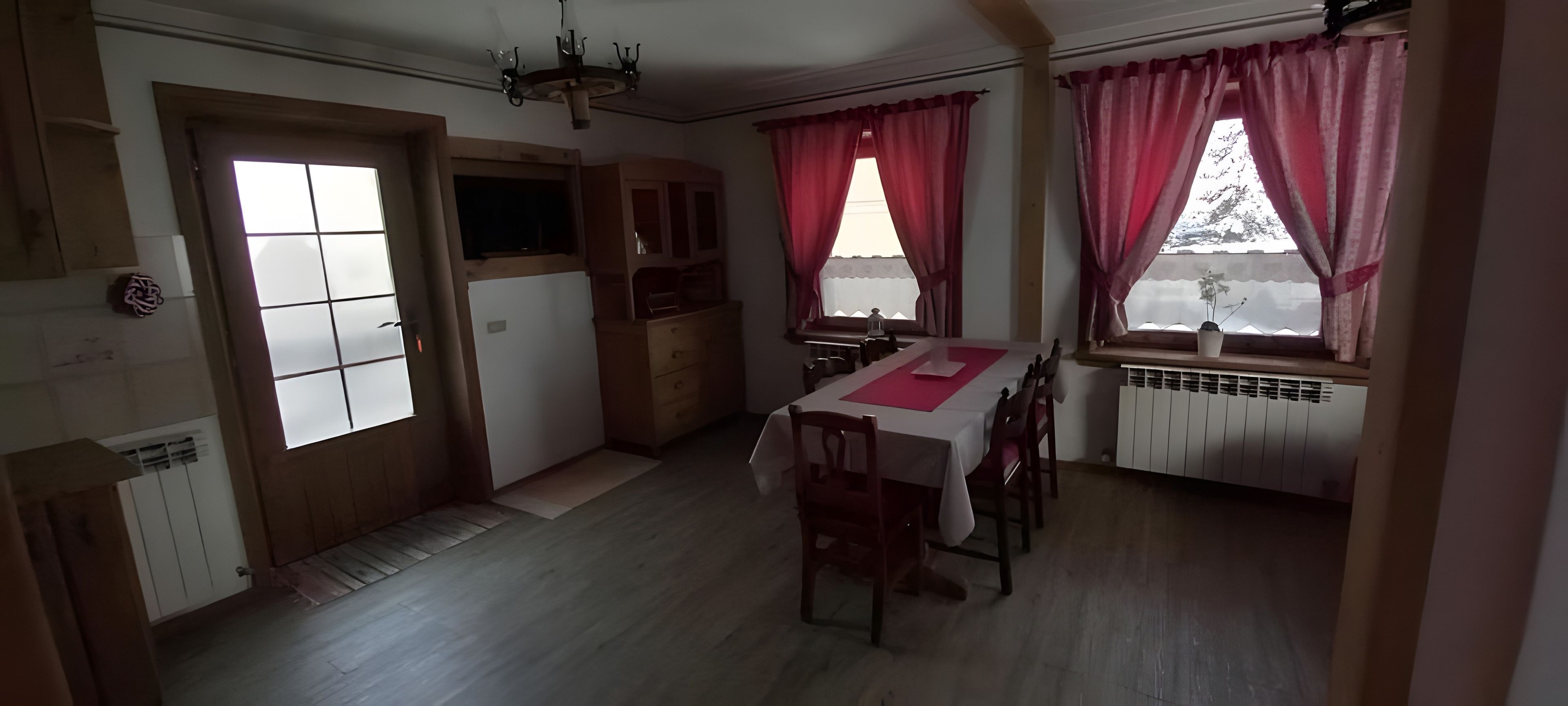 Un coin repas avec une table dressée pour quatre personnes, un buffet en bois et une fenêtre avec des rideaux.