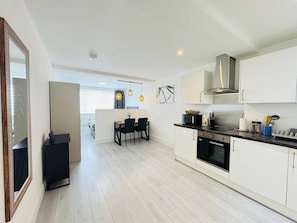 Een moderne keuken met witte kasten, een roestvrijstalen afzuigkap en een eethoek met een tafel en stoelen.