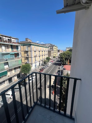 Un balcón con vista a una calle de la ciudad, edificios y coches aparcados.