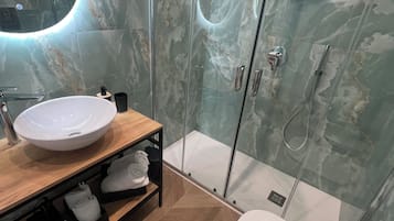 A modern bathroom with a marble shower enclosure, a round mirror, a wooden vanity with a sink, and a toilet.