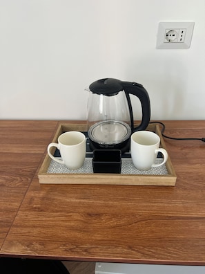 Una cafetera sobre una bandeja con dos tazas blancas, un enchufe en la pared y una mesa de madera.