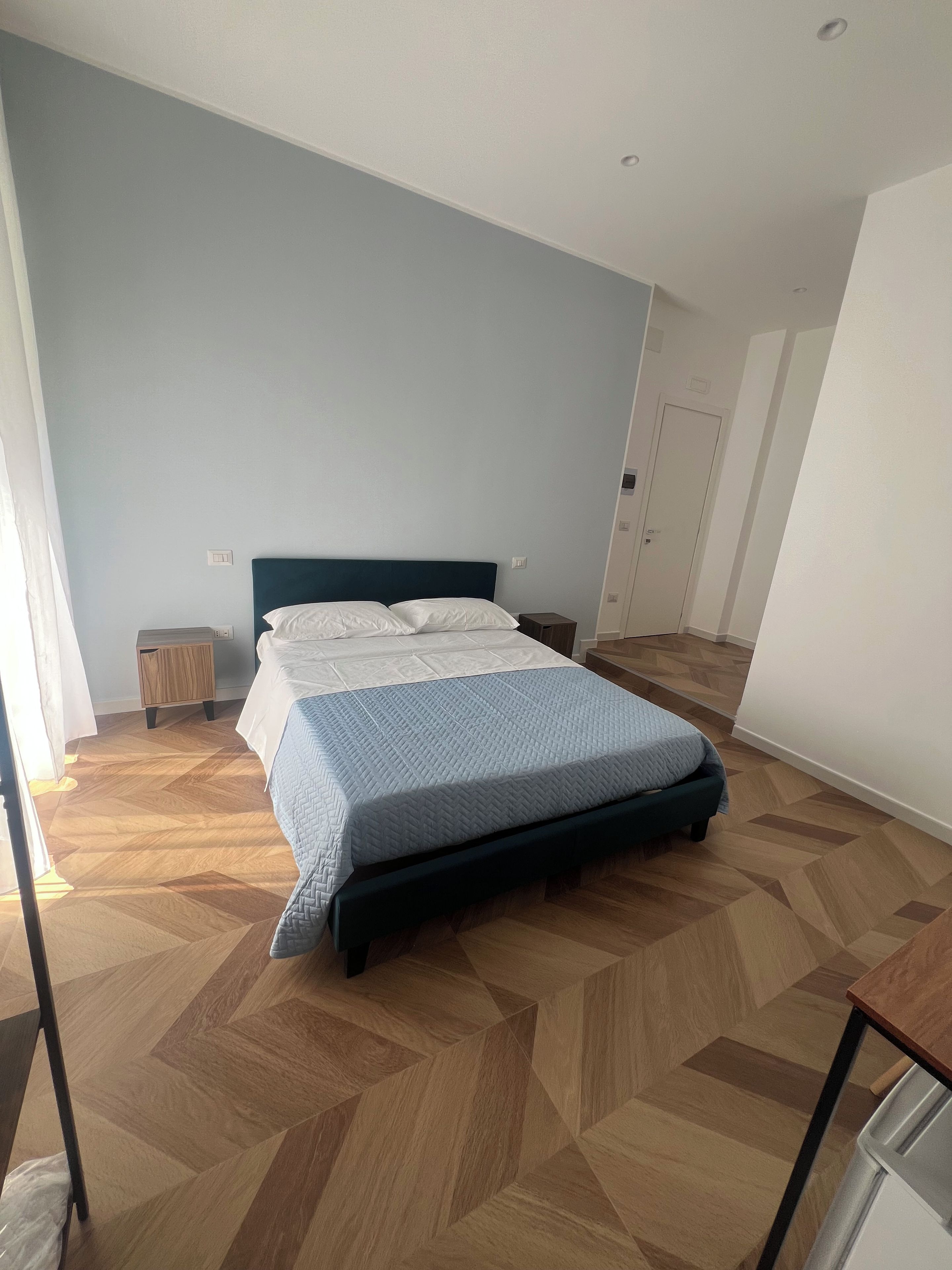 A bedroom with a bed, a bedside table, a wardrobe, and a door.