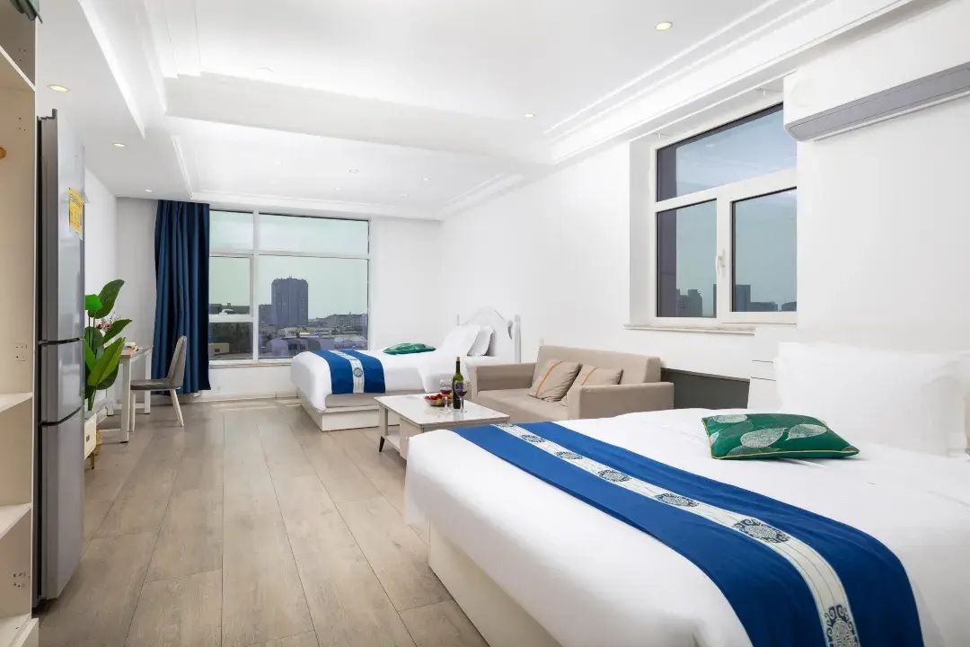 A hotel room with a bed, a sofa, a desk, and a view of the city.