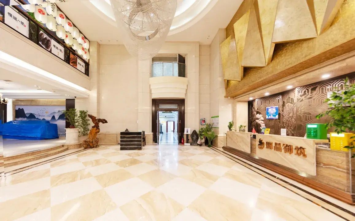 A hotel lobby with a check-in counter, a reception desk, and a staircase leading to an upper floor.