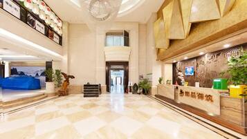 A hotel lobby with a check-in counter, a reception desk, and a staircase leading to an upper floor.
