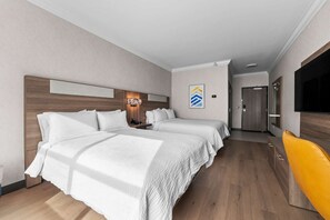 Hotellihuone, jossa on kaksi sänkyä, puinen pääty, seinälle asennettu televisio ja ovi, joka johtaa käytävään.