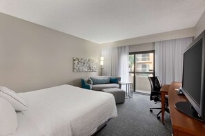 Ein Hotelzimmer mit Bett, Schreibtisch, Fernseher, Stuhl und Blick ins Freie.