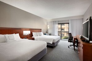 Ein Hotelzimmer mit zwei Betten, einem Schreibtisch, einem Fernseher und Blick ins Freie.