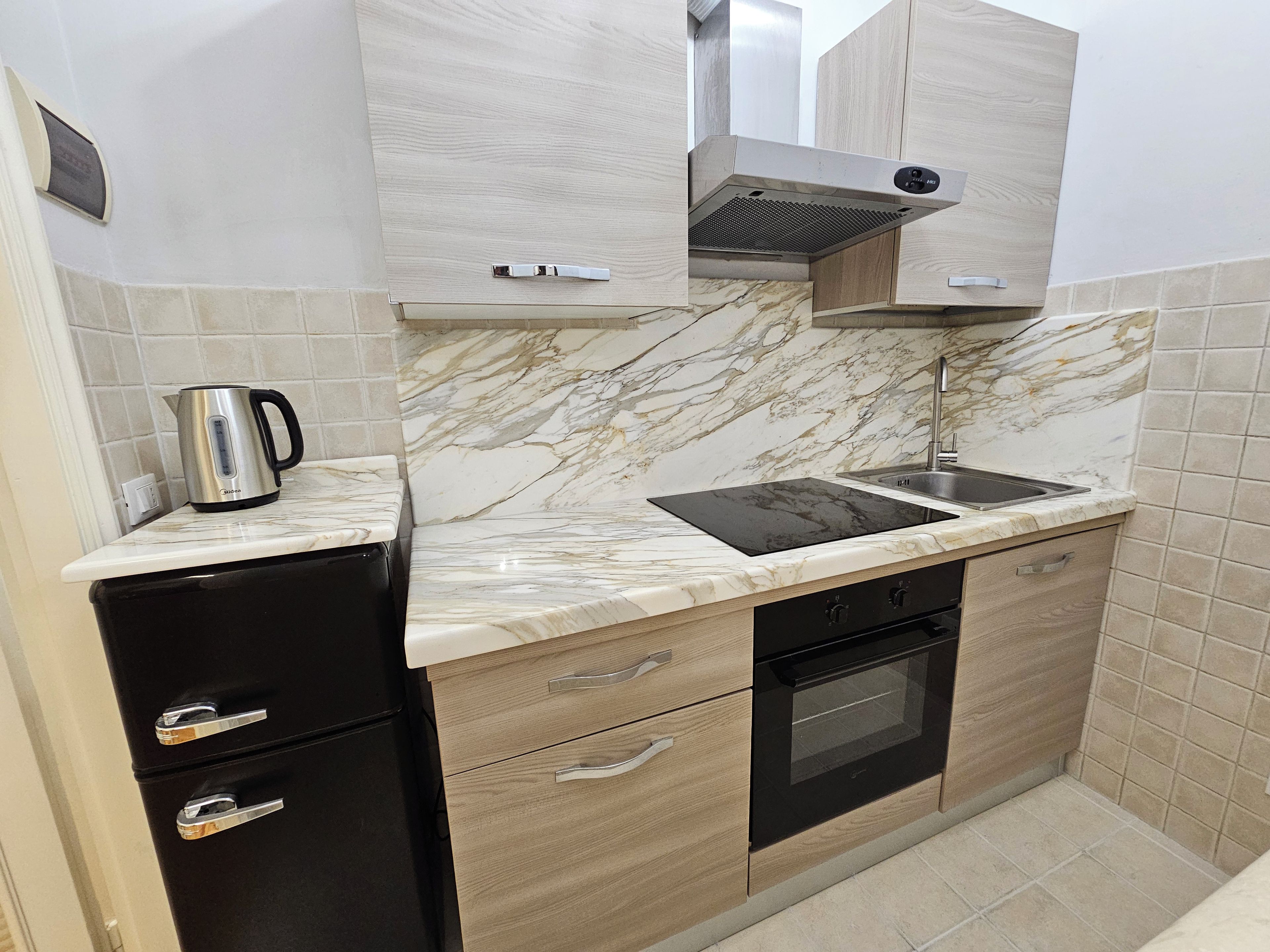 A compact kitchen with a built-in stove, oven, and sink, featuring marble backsplash and wooden cabinetry.