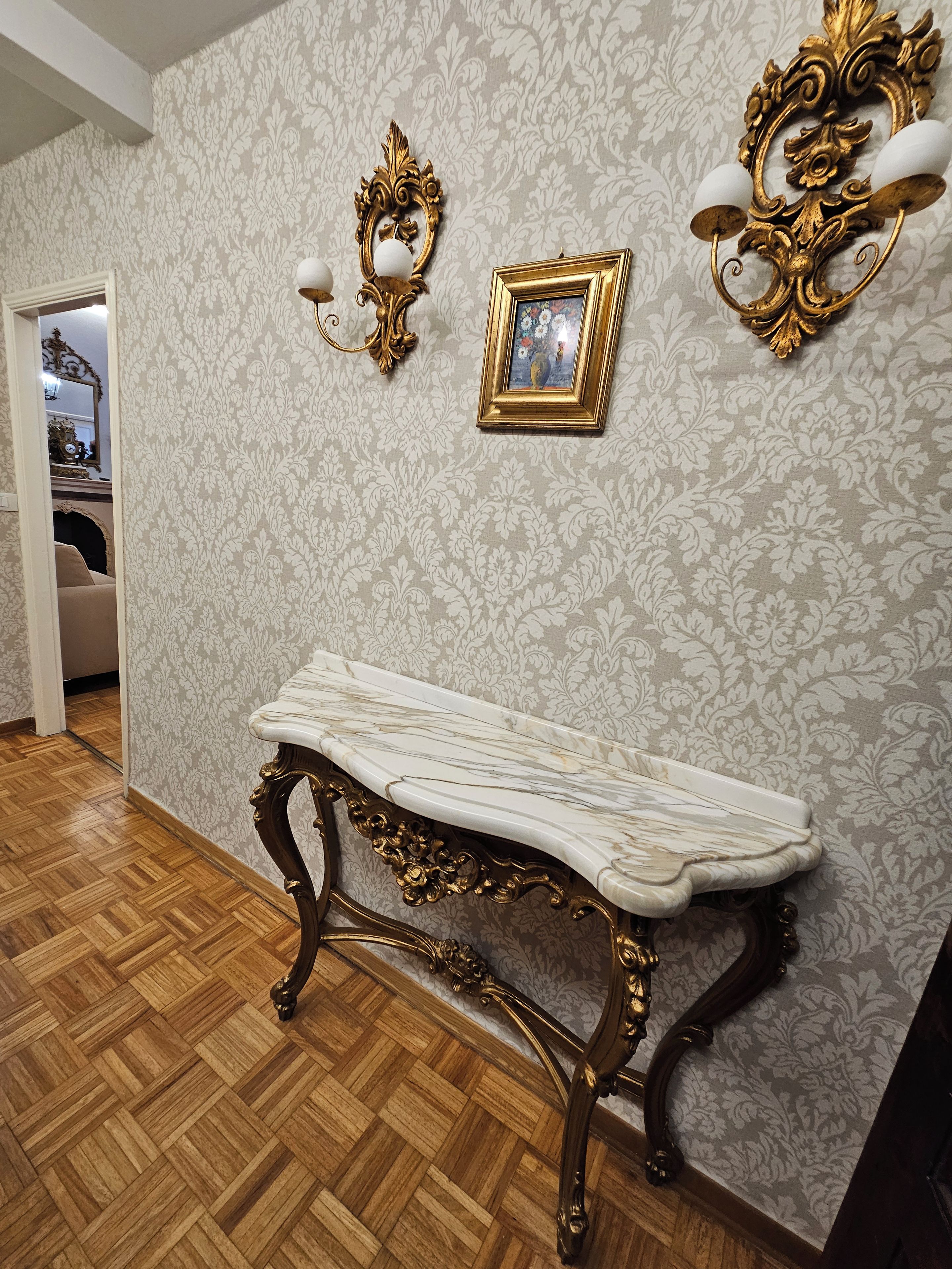 A room with a marble table, ornate wall sconces, and a patterned wallpaper.