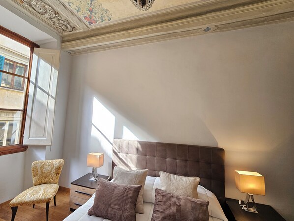 A bedroom with a bed, two bedside tables, a chair, and a window. - New Listing (Firenze)