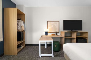 Une chambre d’hôtel équipée d’une armoire, d’un bureau avec une lampe, d’une télévision et d’un lit.