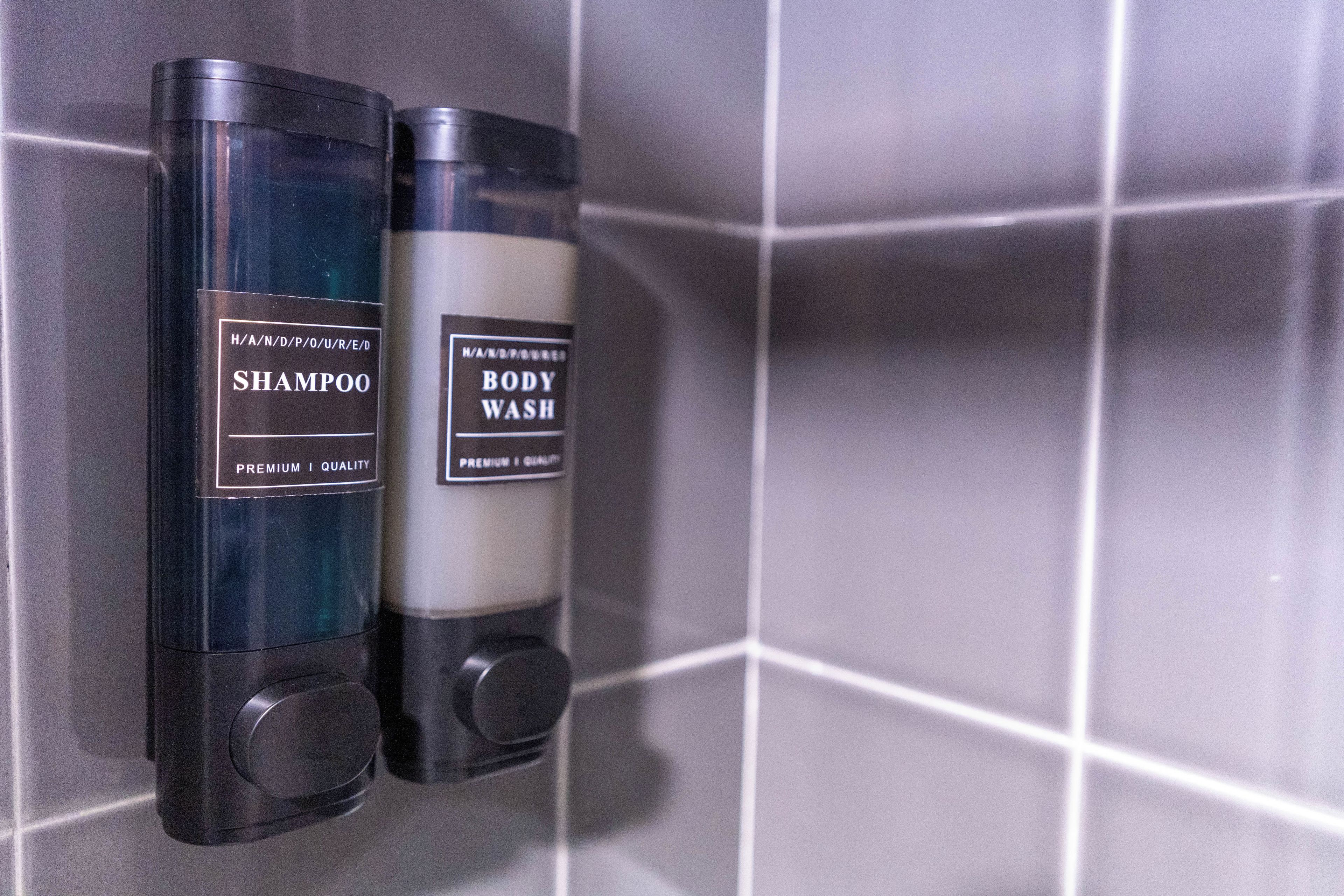 Two bottles of shampoo and body wash on a tiled wall.