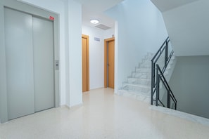 Un pasillo con un ascensor blanco, una puerta de madera y una escalera de mármol.