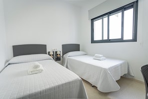 Una habitación con dos camas, cada una con una almohada y una toalla enrollada. Hay mesitas de noche con lámparas.