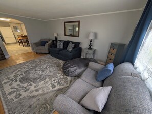 Un salon avec un canapé gris, un tapis à motifs et, au fond, un coin repas.