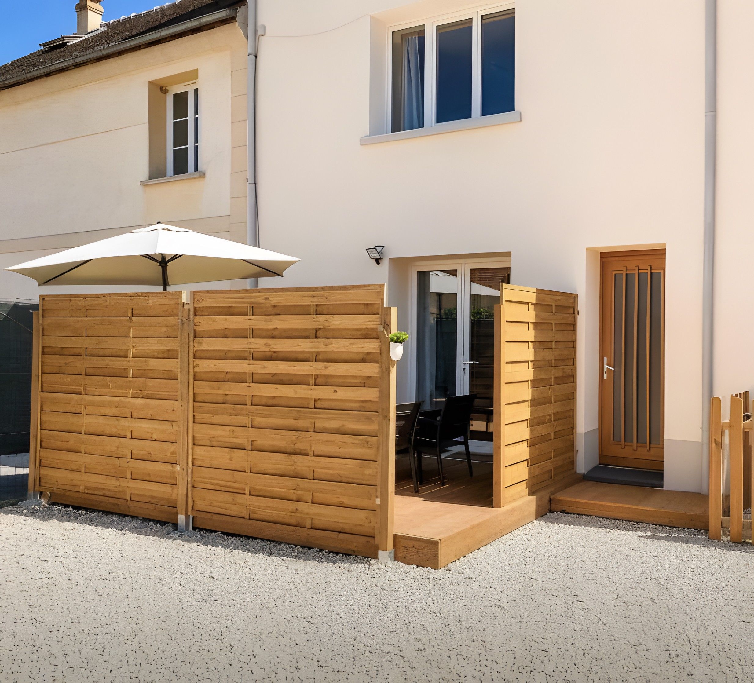 Een overdekt terras met een houten omheining, een tafel en stoelen.