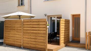 Een overdekt terras met een houten omheining, een tafel en stoelen.