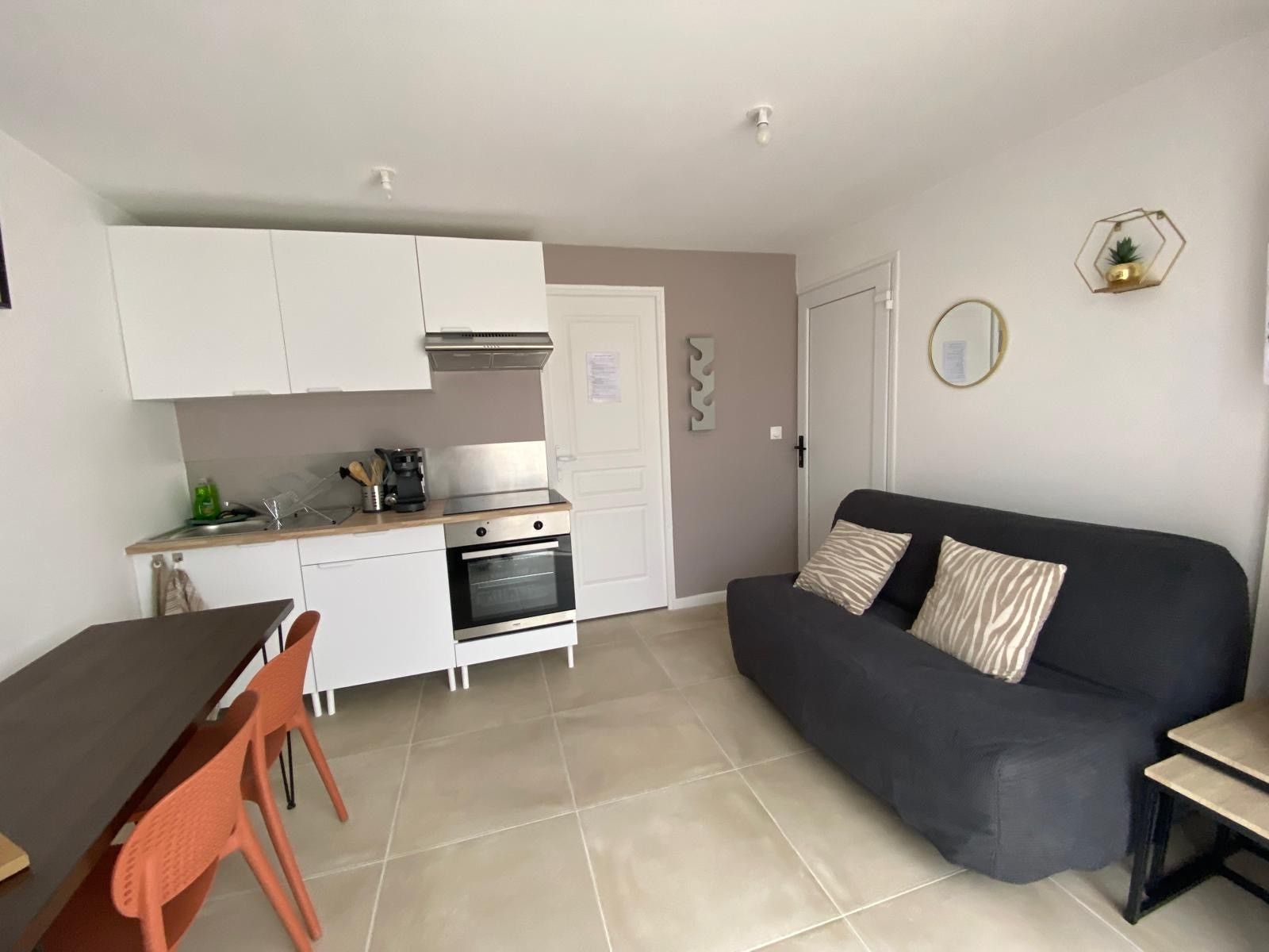 Een compacte leefruimte met een kitchenette, een eethoek met tafel en stoelen, en een bank.