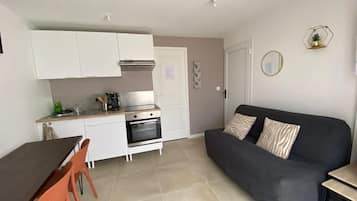 Een compacte leefruimte met een kitchenette, een eethoek met tafel en stoelen, en een bank.