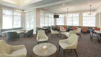 A hotel lobby with a mix of seating options including sofas and chairs, a coffee table, and a television screen mounted on the wall.