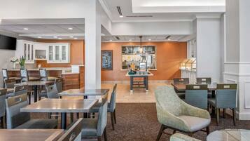 A hotel lobby with a dining area, a reception desk, and a kitchen in the background.