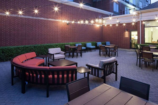 An outdoor seating area with brick walls, string lights, and various seating options including sofas and tables. - Close to Allen Premium Outlets + Onsite Dining (Allen)