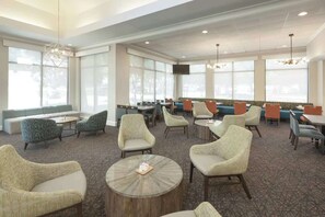 Un hall d’hôtel offrant différents types de sièges, notamment des canapés et des fauteuils, une table basse et un écran de télévision fixé au mur.