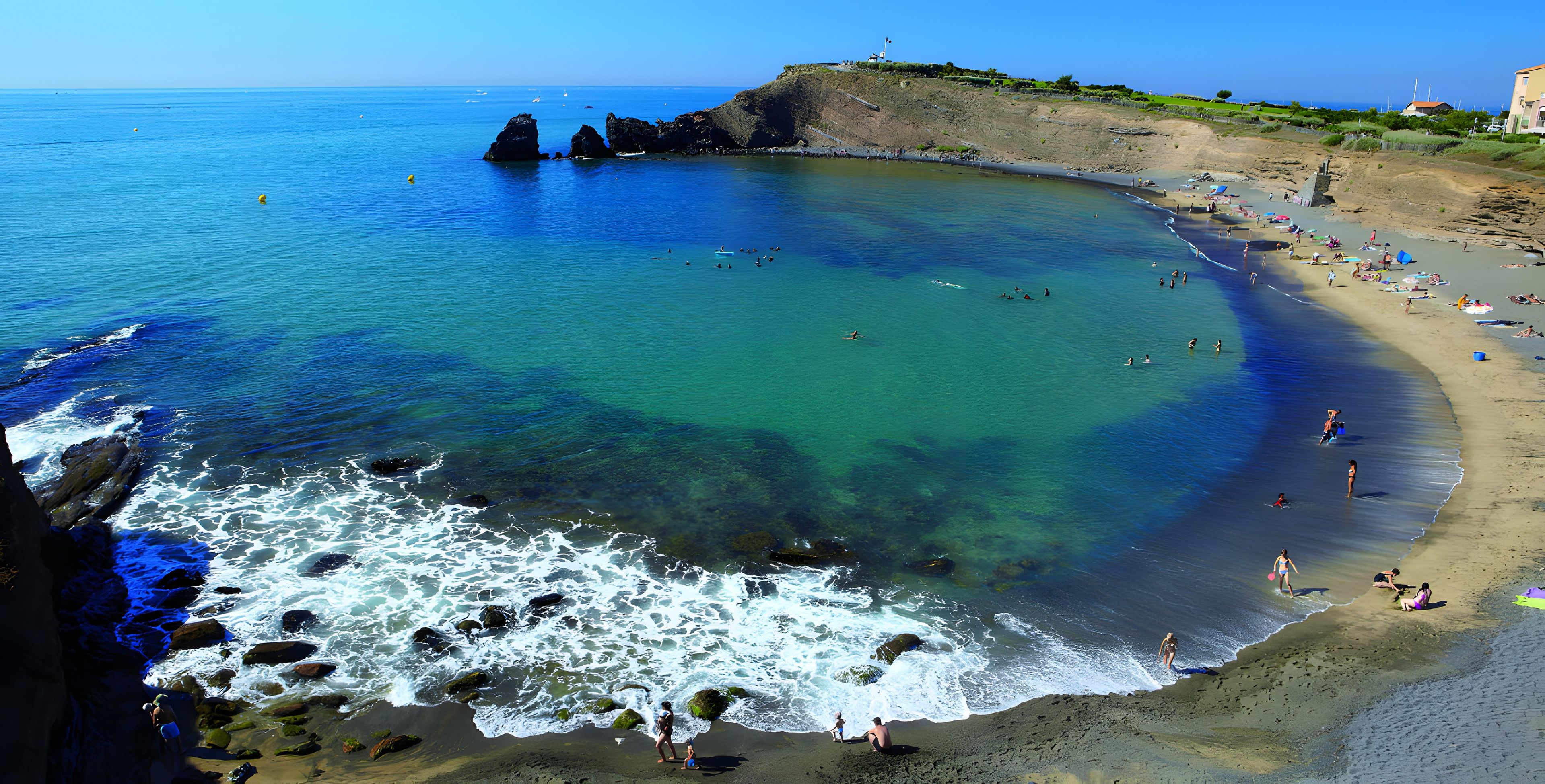 A beach with clear water, rocky shoreline, and people swimming and sunbathing.
