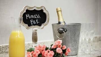 Een barruimte met een bord waarop 'Mimasa Bar' staat, een champagnefles in een metalen emmer en een glas jus d'orange.