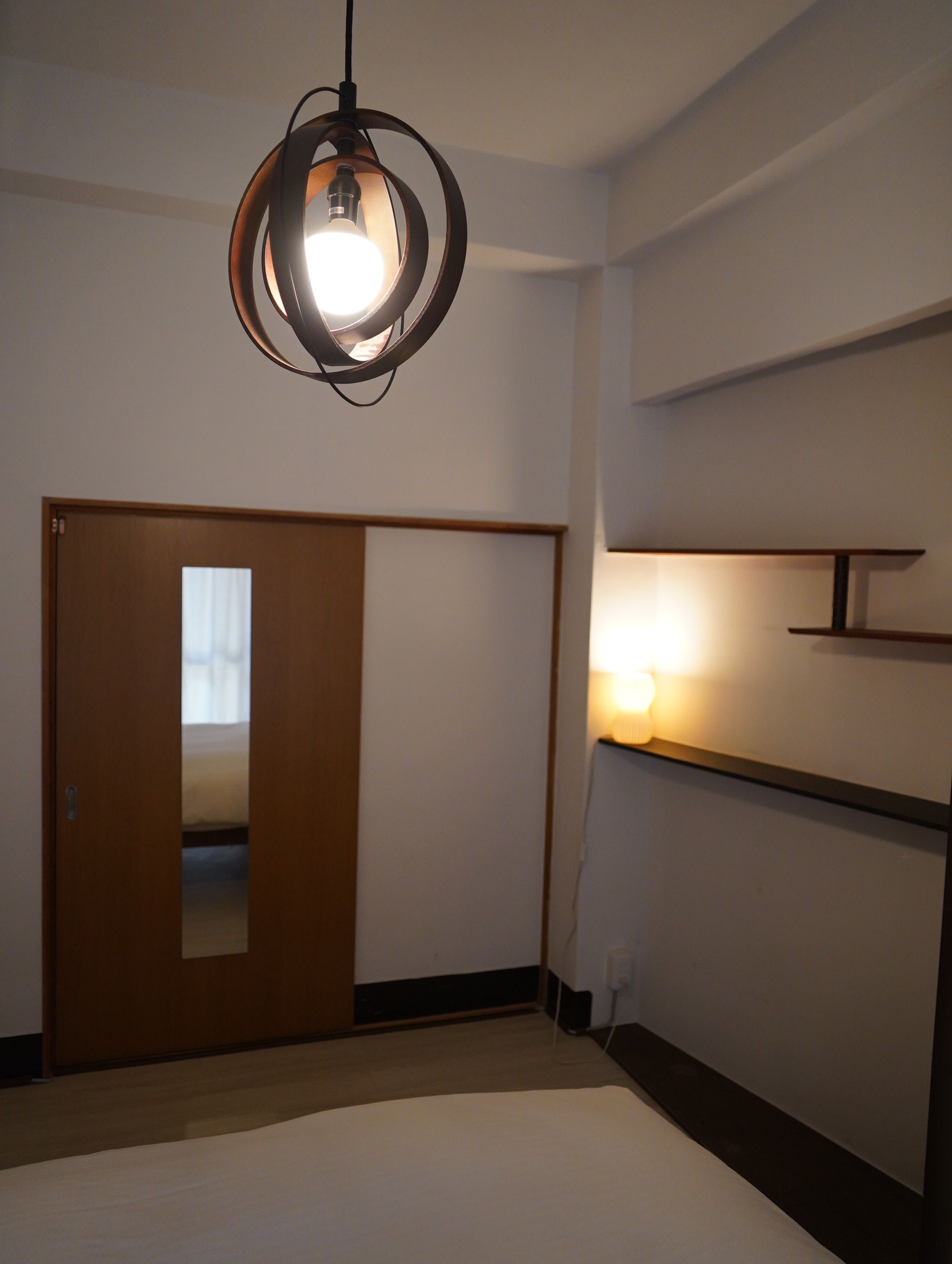 A room with a bed, a wardrobe, a wall-mounted shelf, and a circular light fixture.