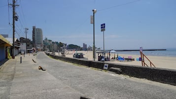 A coastal road with beachside buildings, a clear sky, and a beach with umbrellas and chairs.