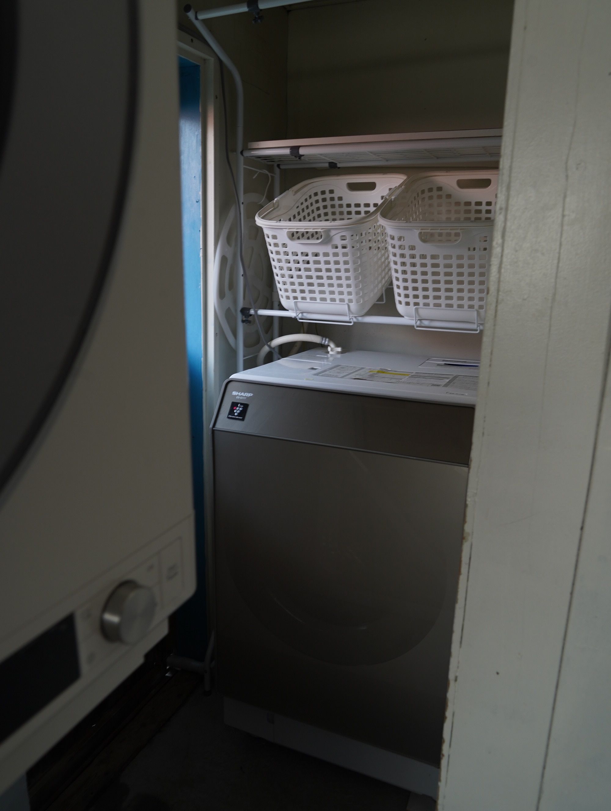 A compact, built-in washing machine with a control panel and a shelf above it holding two white laundry baskets.