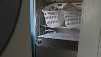 A compact, built-in washing machine with a control panel and a shelf above it holding two white laundry baskets.