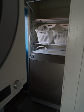 A compact, built-in washing machine with a control panel and a shelf above it holding two white laundry baskets. - New Listing (南知多町)