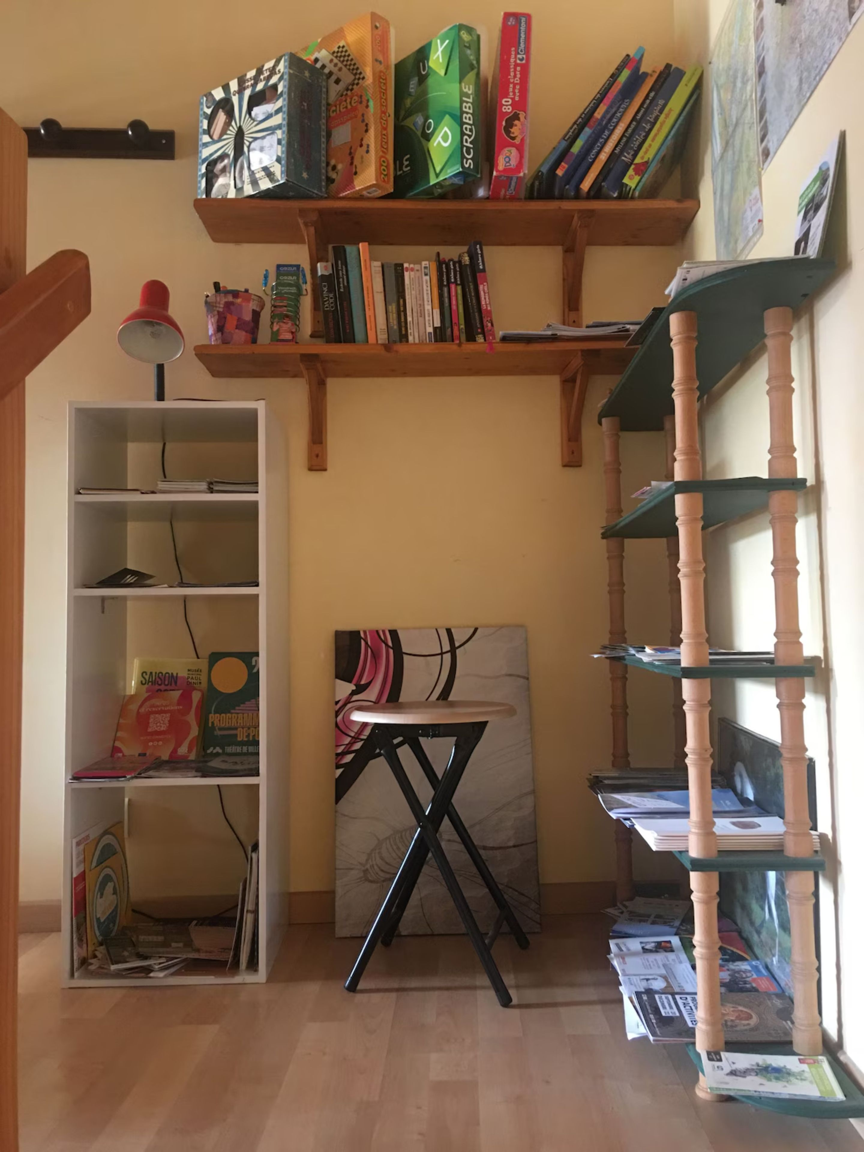 Una habitación con un escritorio, estanterías con libros y juegos, una lámpara y un cuadro.