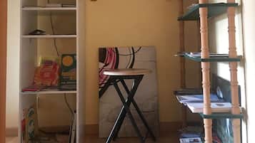 Una habitación con un escritorio, estanterías con libros y juegos, una lámpara y un cuadro.