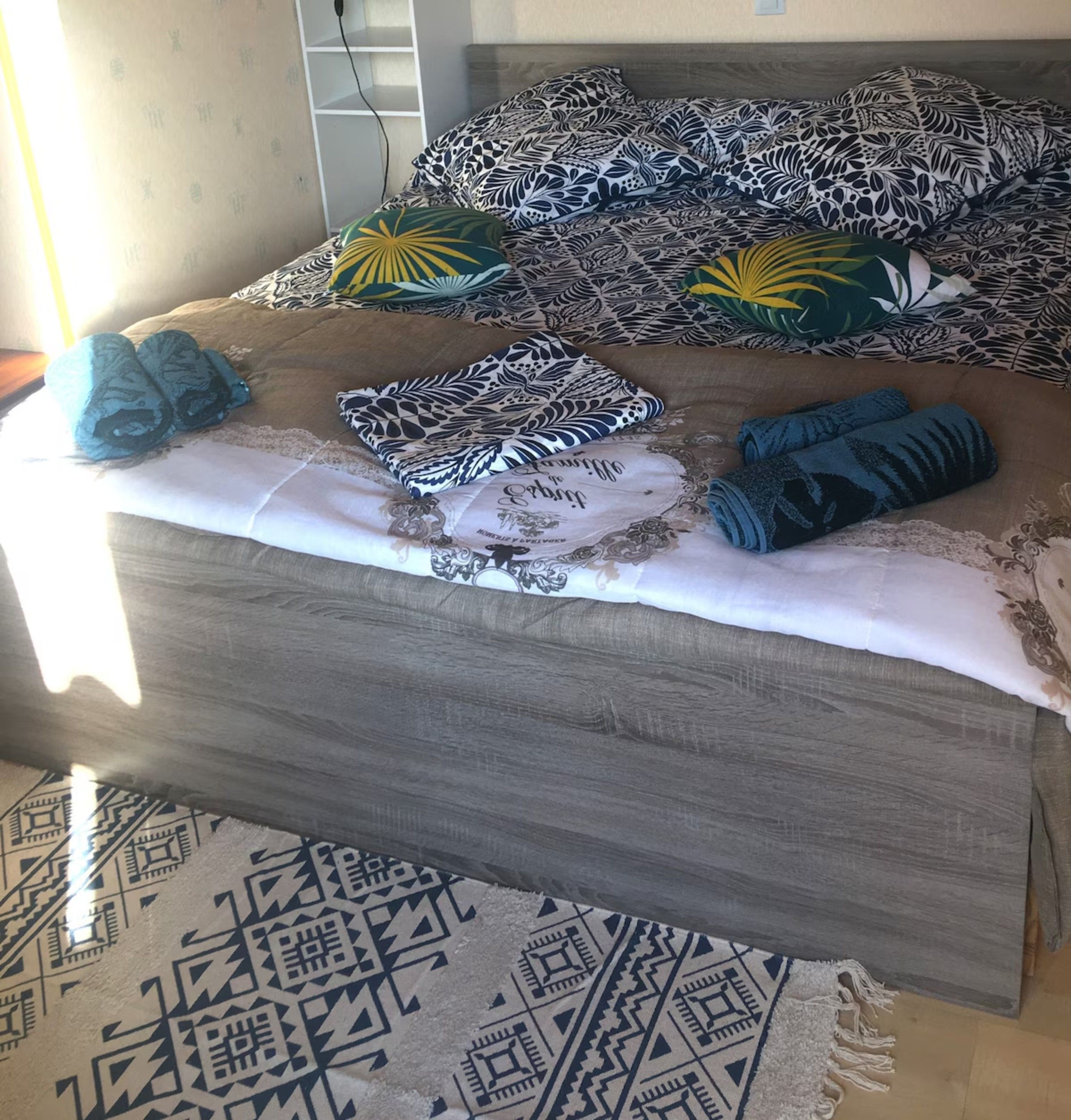 Un lit avec une literie à motifs, un coussin décoratif et un tapis aux motifs géométriques.