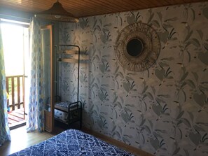 Une pièce comprenant un lit, un fauteuil suspendu, un grand miroir rond fixé au mur et un papier peint à motifs.