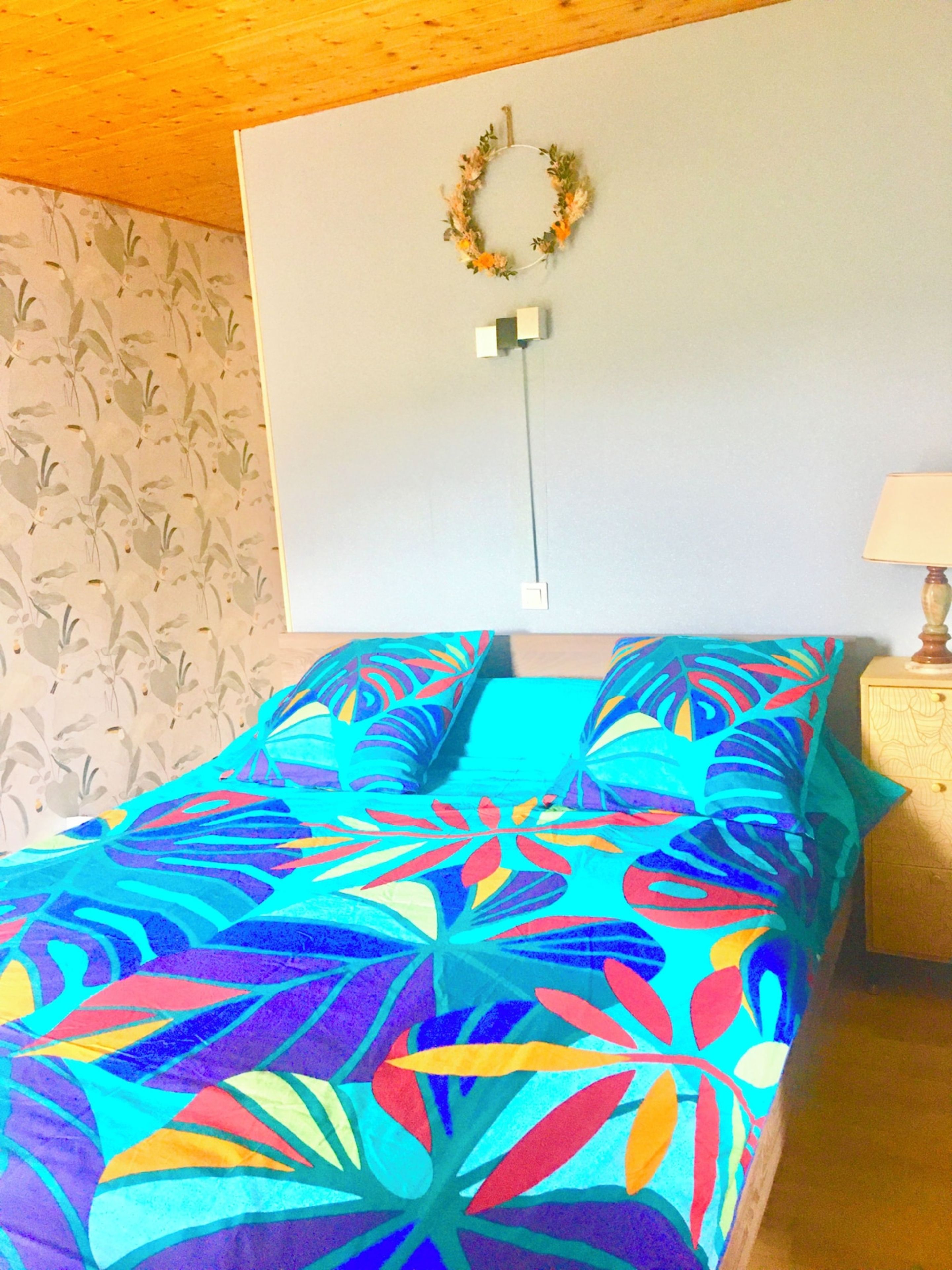 A room with a bed, a wall-mounted light switch, and a wall with a floral pattern.