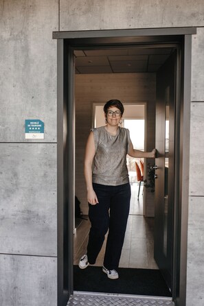 Une personne se tient dans l’encadrement d’une porte, tenant une pancarte indiquant un établissement lié au tourisme.