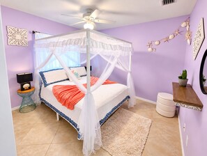 A bedroom with a four-poster canopy bed, a bedside table with a lamp, a small potted plant, and decorative wall art. - Family Nest Pool&Gulf Coast Aventures (North Port)