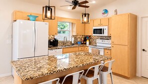 A kitchen with a granite countertop, white appliances, wooden cabinets, and a ceiling fan. - Family Nest Pool&Gulf Coast Aventures (North Port)