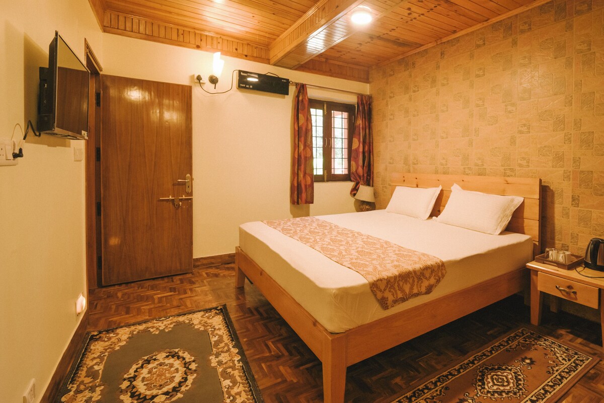 A bedroom with a wooden bed, a nightstand, a wall-mounted TV, and a patterned rug.