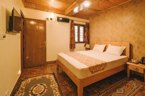 A bedroom with a wooden bed, a nightstand, a wall-mounted TV, and a patterned rug. - The Willow Way (Nainital)
