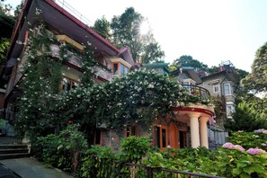 A multi-story building with a balcony, surrounded by lush greenery and flowering plants. - The Willow Way (Nainital)