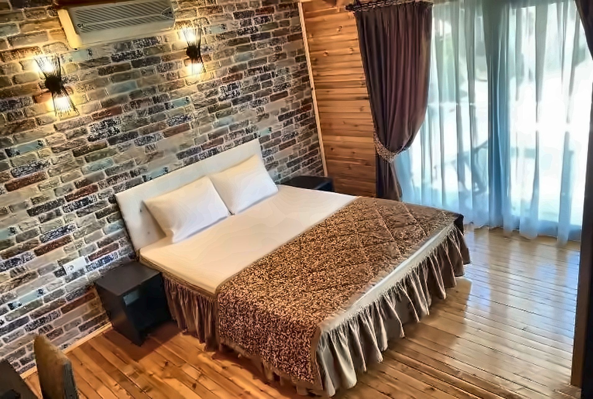 A bedroom with a brick wall, a bed with a patterned bedspread, and a window with curtains.