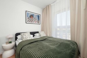 A bedroom with a bed, a bedside lamp, a potted plant, and a framed picture on the wall. - Łódź | Srebrzyńska 12 | Modern Apartment | Air conditioning | Parking (Łódź)
