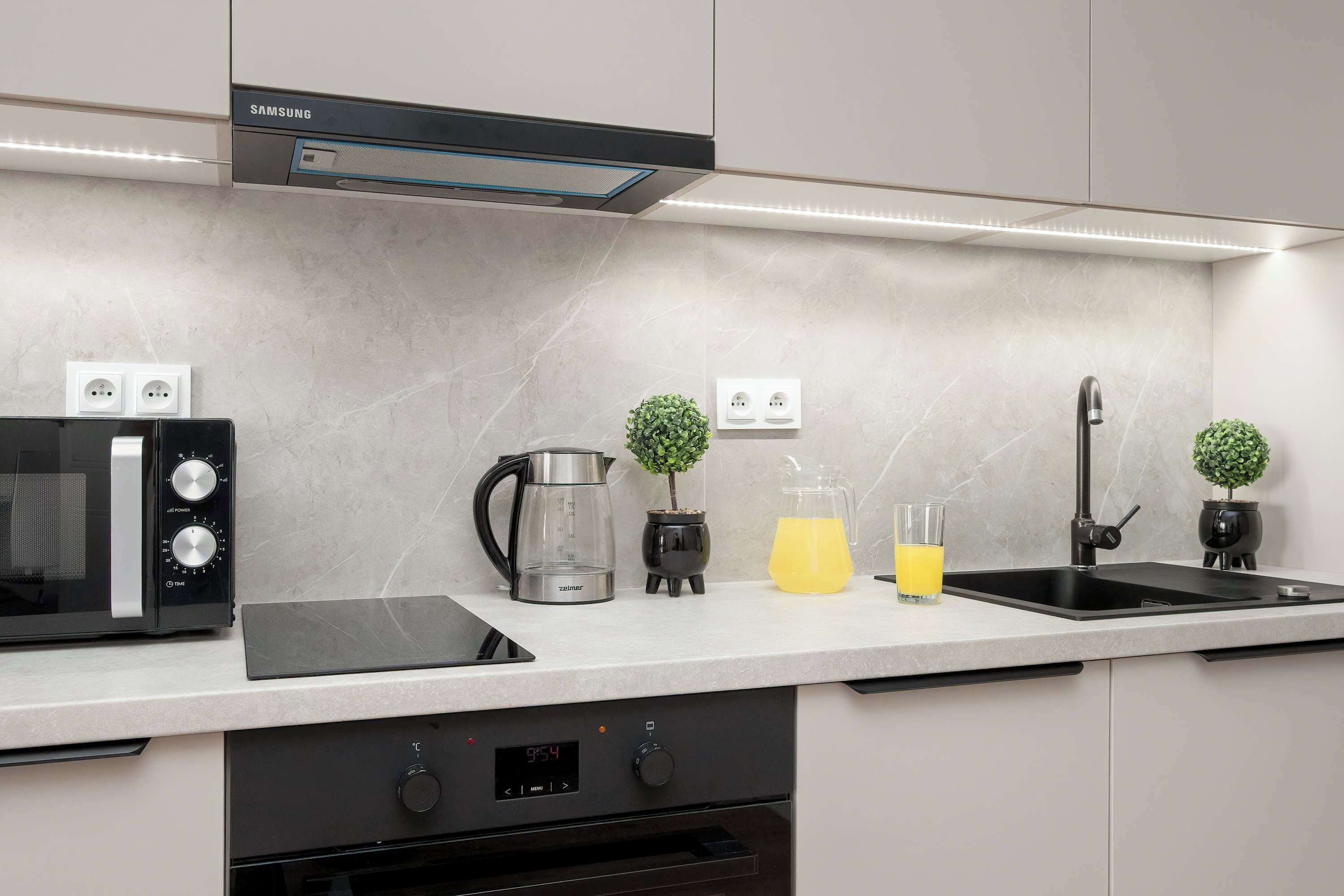 Een moderne keuken met een inbouwoven, waterkoker, koffiezetapparaat, spoelbak en kookplaat.